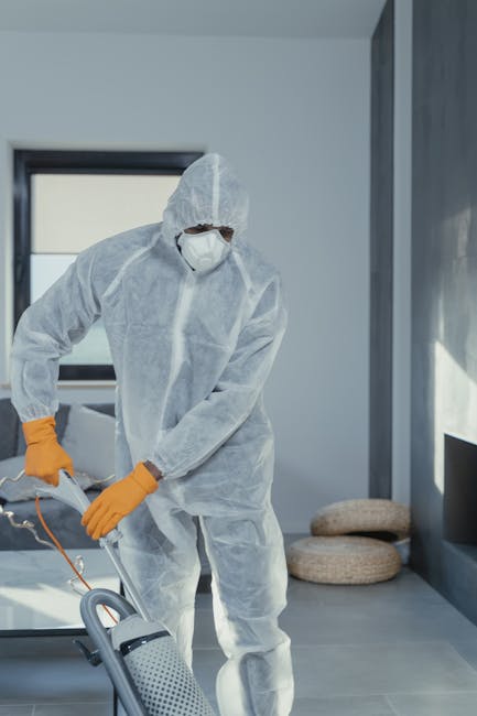 Close-up image showing a professional carpet cleaner's gloved hand operating a carpet cleaning machine with a spray nozzle, applying deep cleaning to a dark, stained carpeted floor inside a residentia